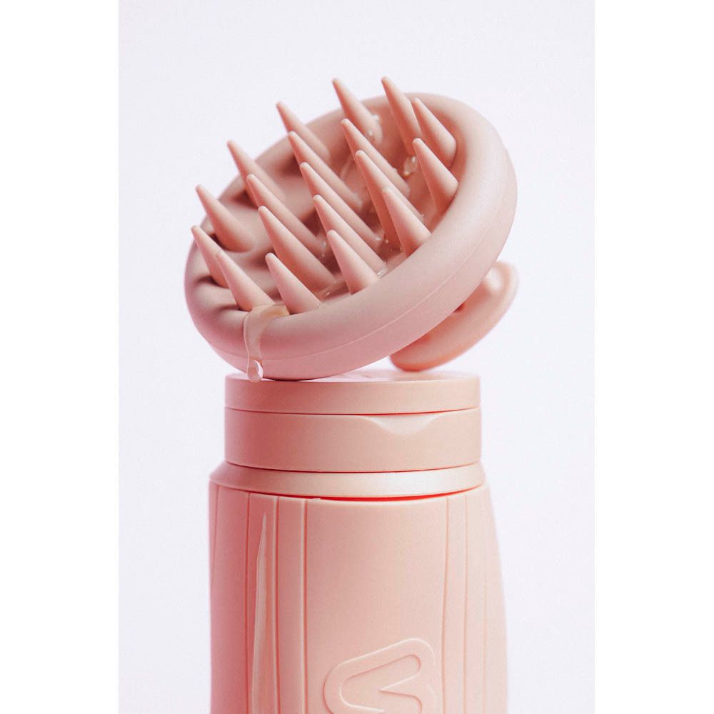 Masseur de cuir chevelu rose en silicone sur flacon rose. Goutte sur l'appareil.