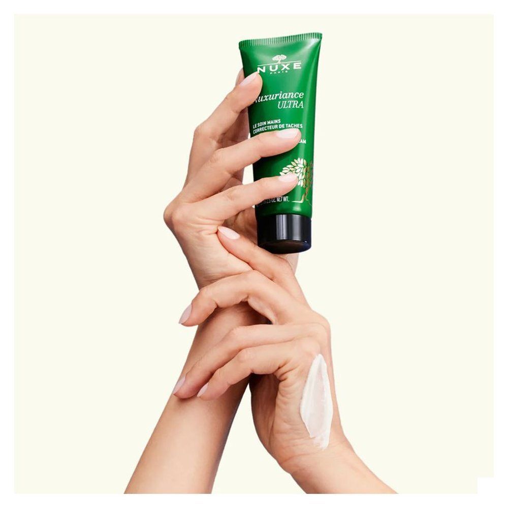 Mains tenant un tube NUXE Nuxuriance Ultra Crème Mains, une trace de crème sur le dos de la main.
