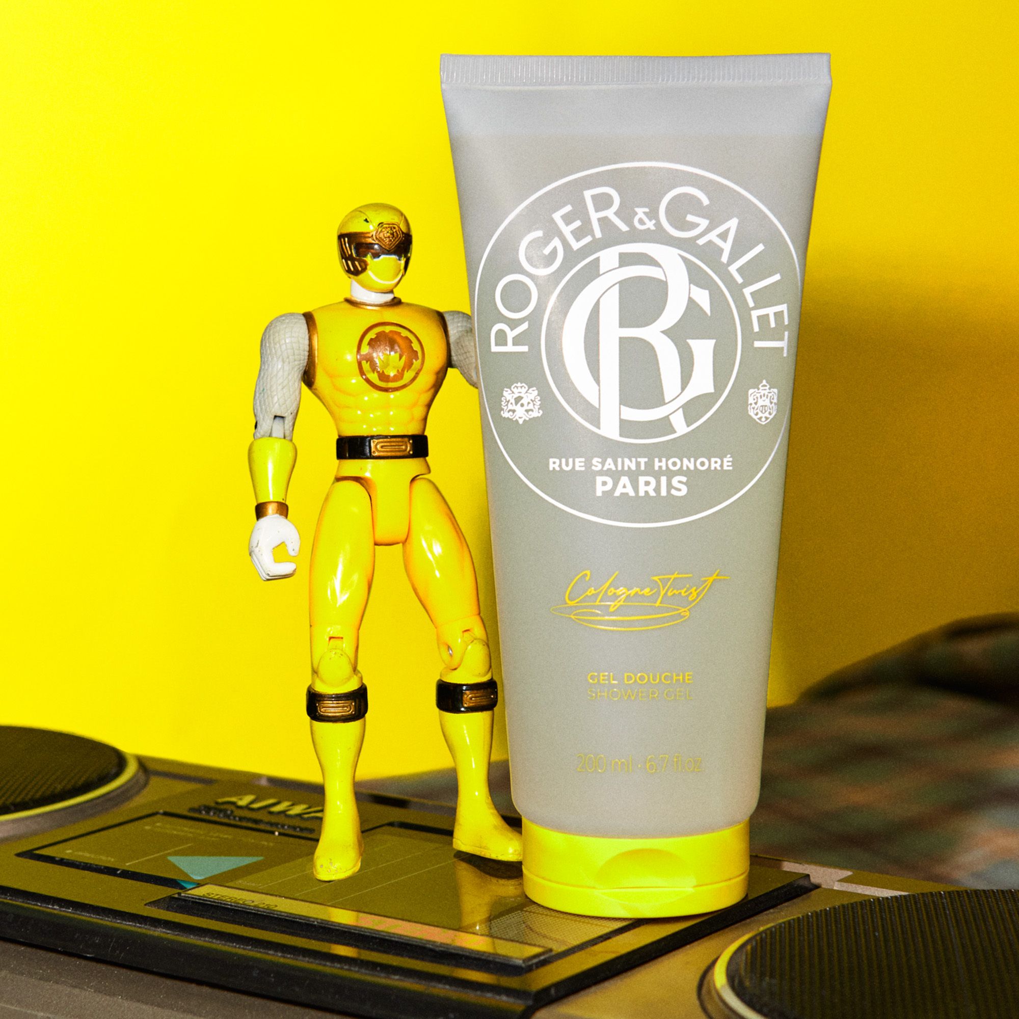 Tube grise avec bouchon jaune. Inscription Roger & Gallet, Cologne Twist, Gel Douche. 200ml. À côté d'une figurine jaune.