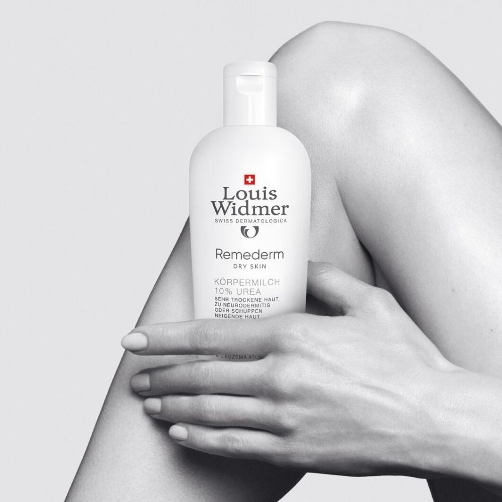 Femme tenant un flacon blanc. Inscriptions: Louis Widmer, Remederm, 10% Urée. Croix suisse.