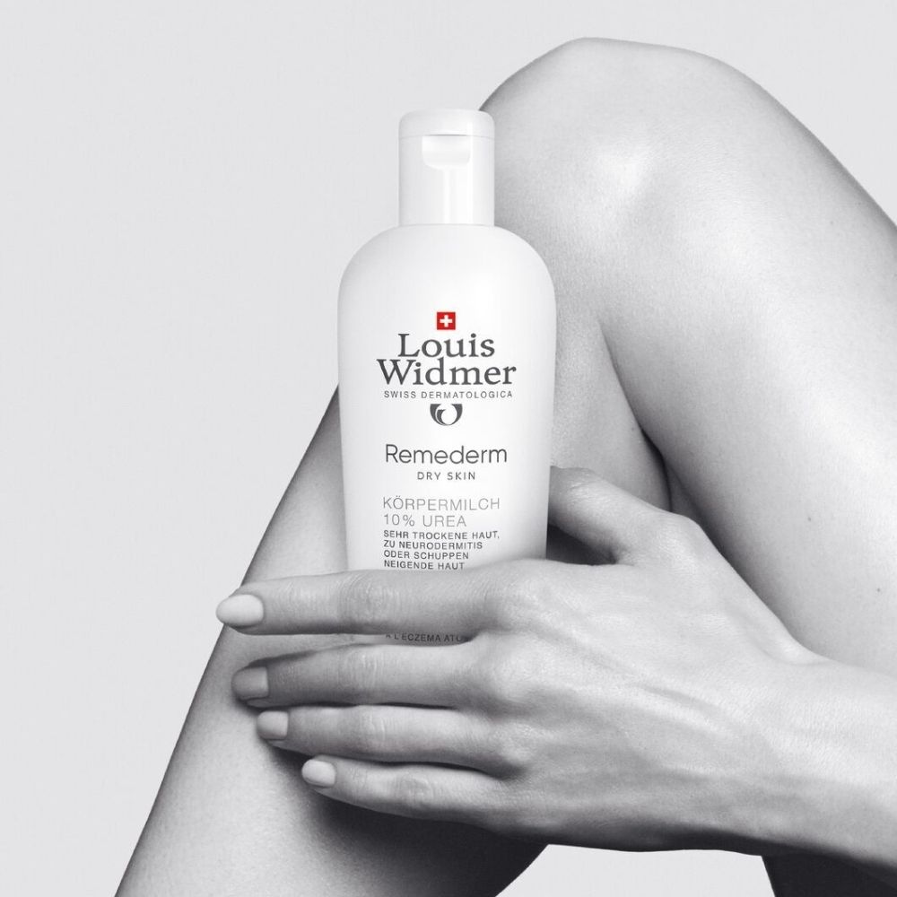 Photo en noir et blanc. Femme avec flacon LOUIS WIDMER Remederm Lait Corporel 10% Urée. Peau sèche.