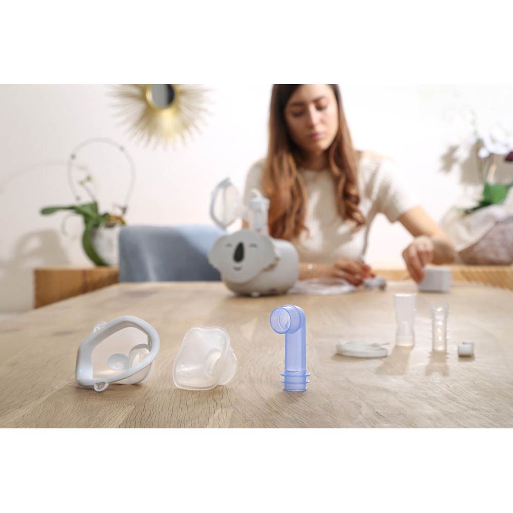 Nébuliseur Koala et accessoires sur table. Différentes pièces. Fond : bois.