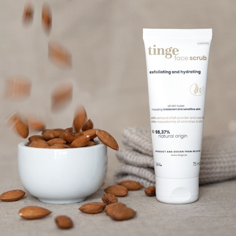Tube Tinge Gommage Visage avec des amandes tombant dans un bol. 98,37% d'origine naturelle.