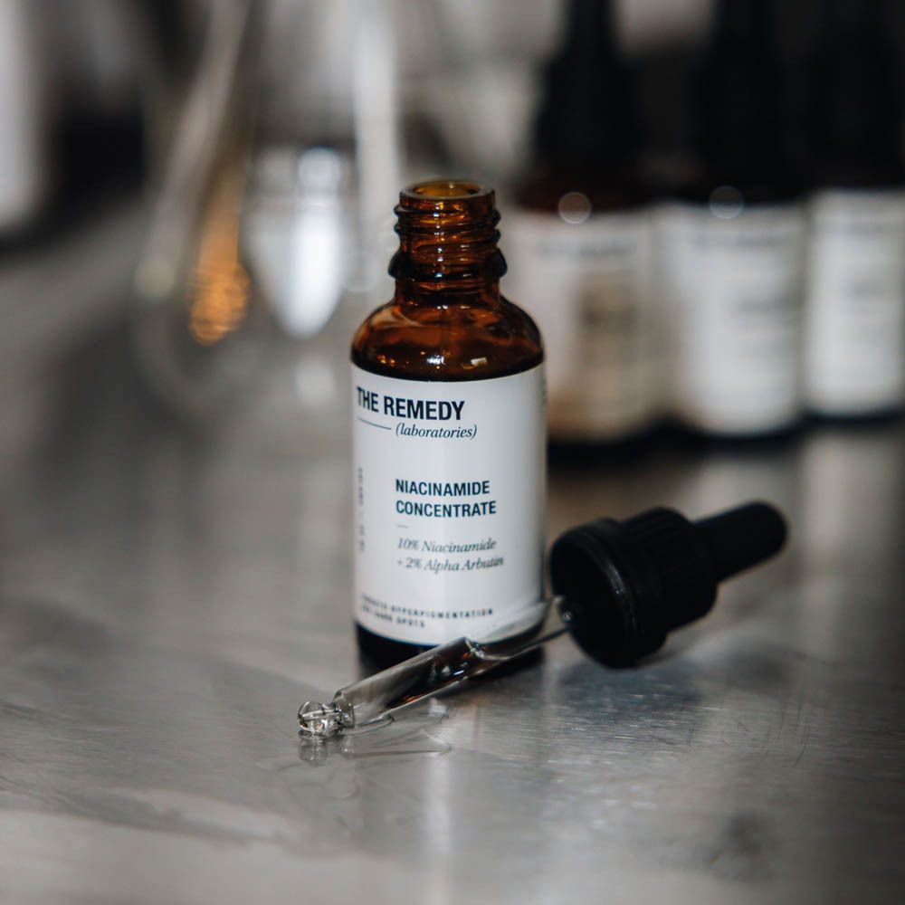 Des mains tiennent un flacon 'THE REMEDY NIACINAMIDE CONCENTRATE' avec pipette.