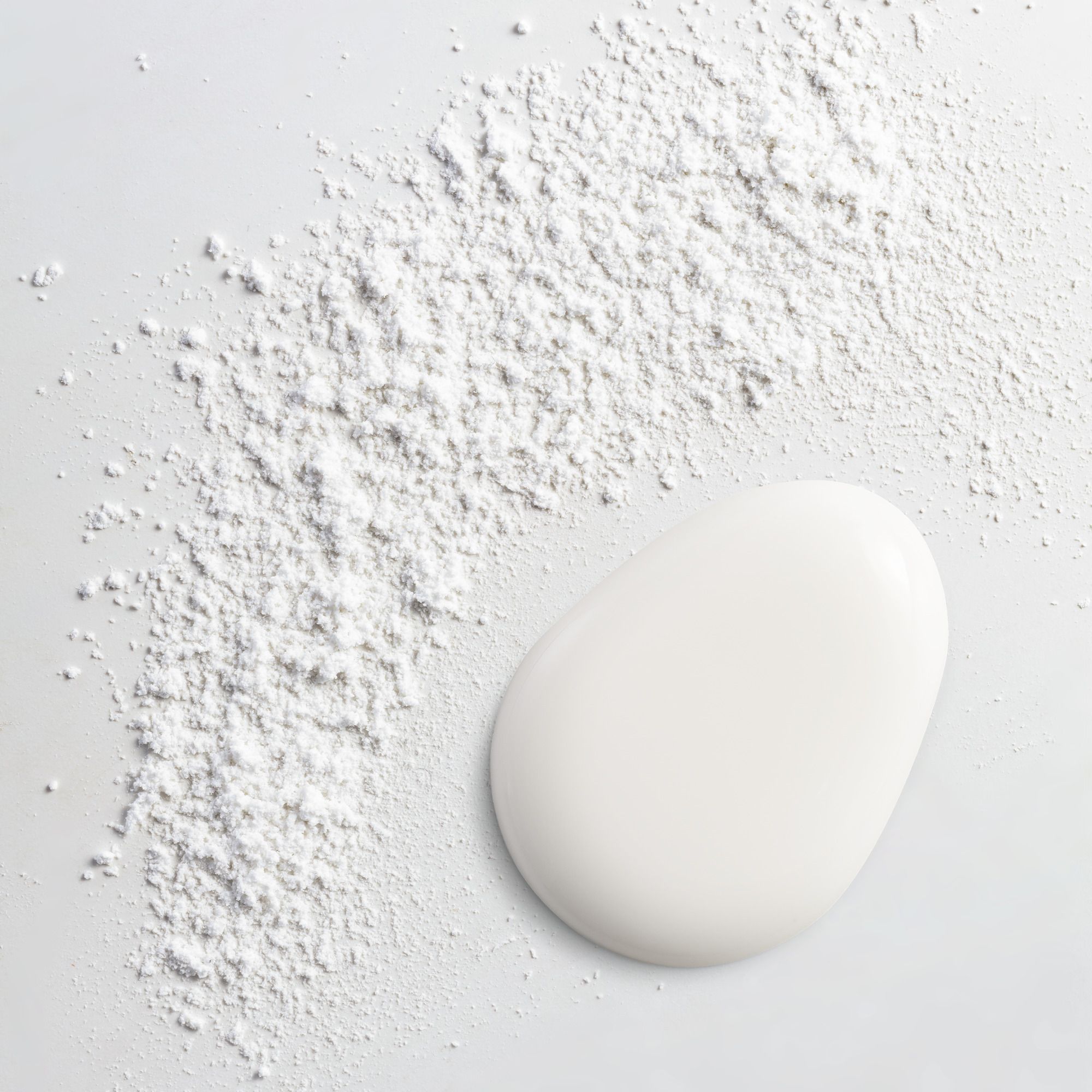 Poudre blanche et liquide blanc sur fond clair. Produit non identifiable.