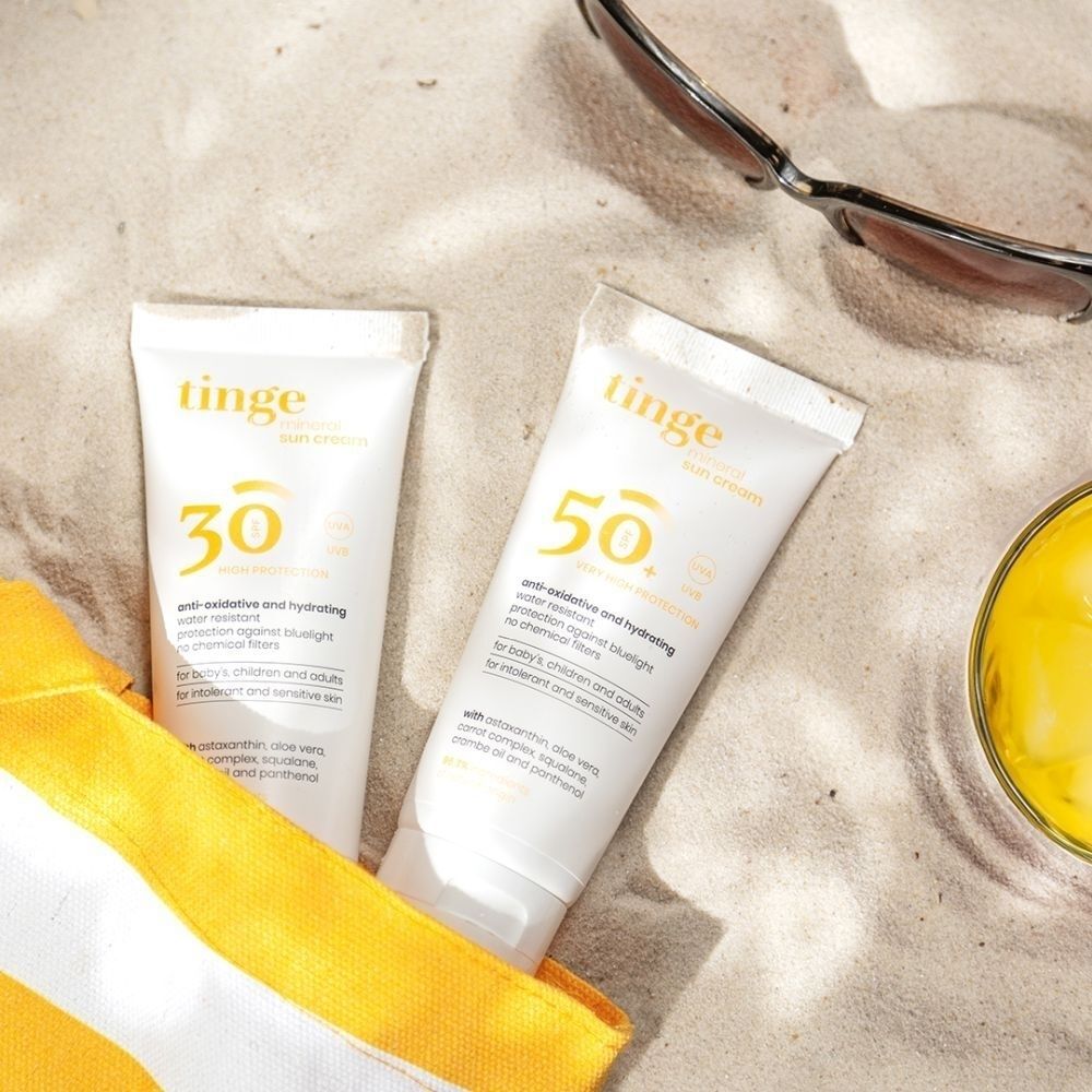 Deux tubes de crème solaire Tinge (SPF30 et SPF50+) sur le sable.