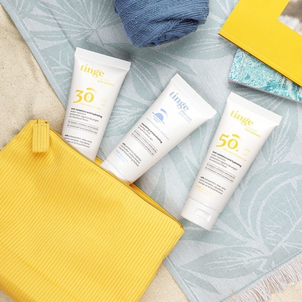Trois tubes de crème solaire Tinge avec pochette sur le sable.
