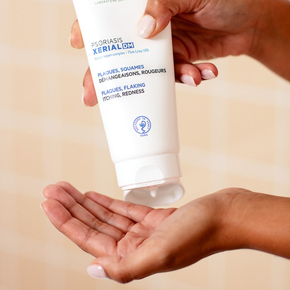 Personne tenant un tube SVR XERIAL DM. Texte: Plaques, Squames, Démangeaisons, Rougeurs. Plaques, Flaking, Itching, Redness. Produit pressé.