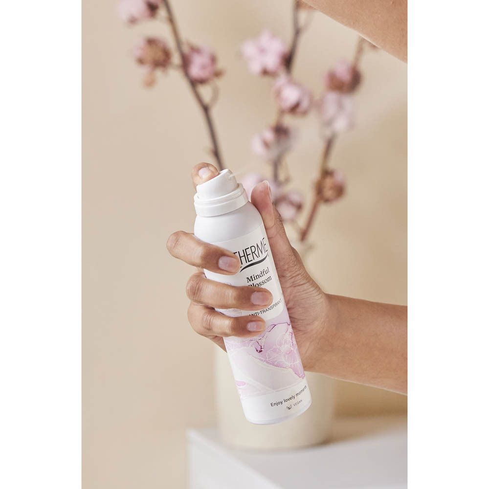 Main tenant le spray Therme Mindful Blossom. Fond : fleurs. Produit tenu.