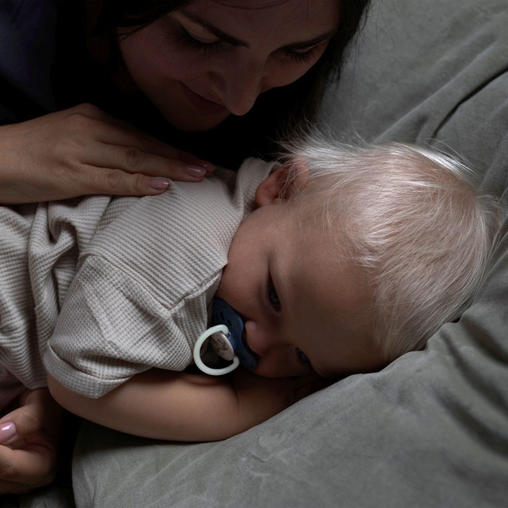 Bébé allongé sur un canapé, sucette en bouche. Mère touchant le bébé. Sucette bleue.
