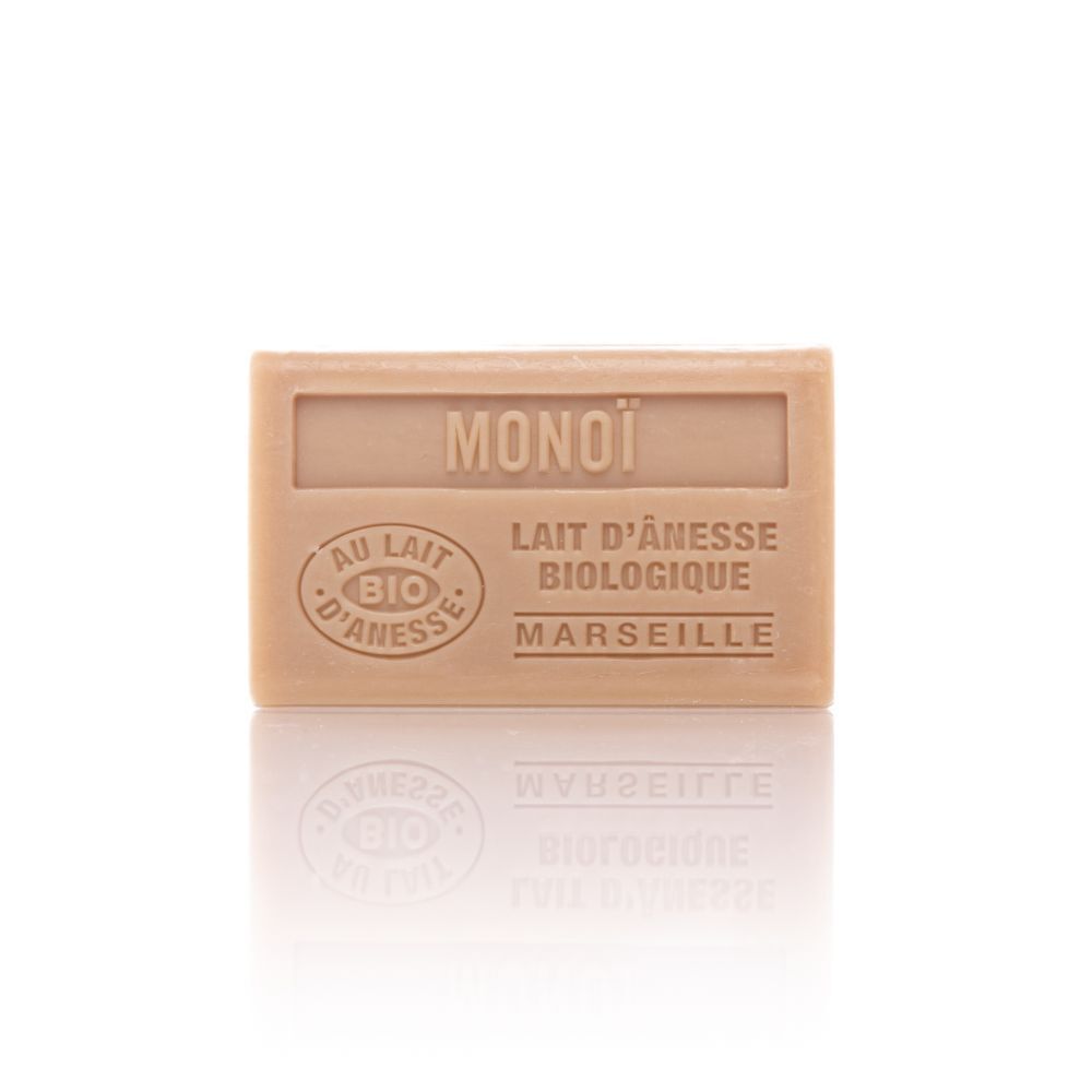 Savon rectangulaire avec inscription MONOÏ, AU LAIT D'ÂNESSE BIOLOGIQUE, MARSEILLE. Certification bio. Couleur claire, surface réfléchissante.
