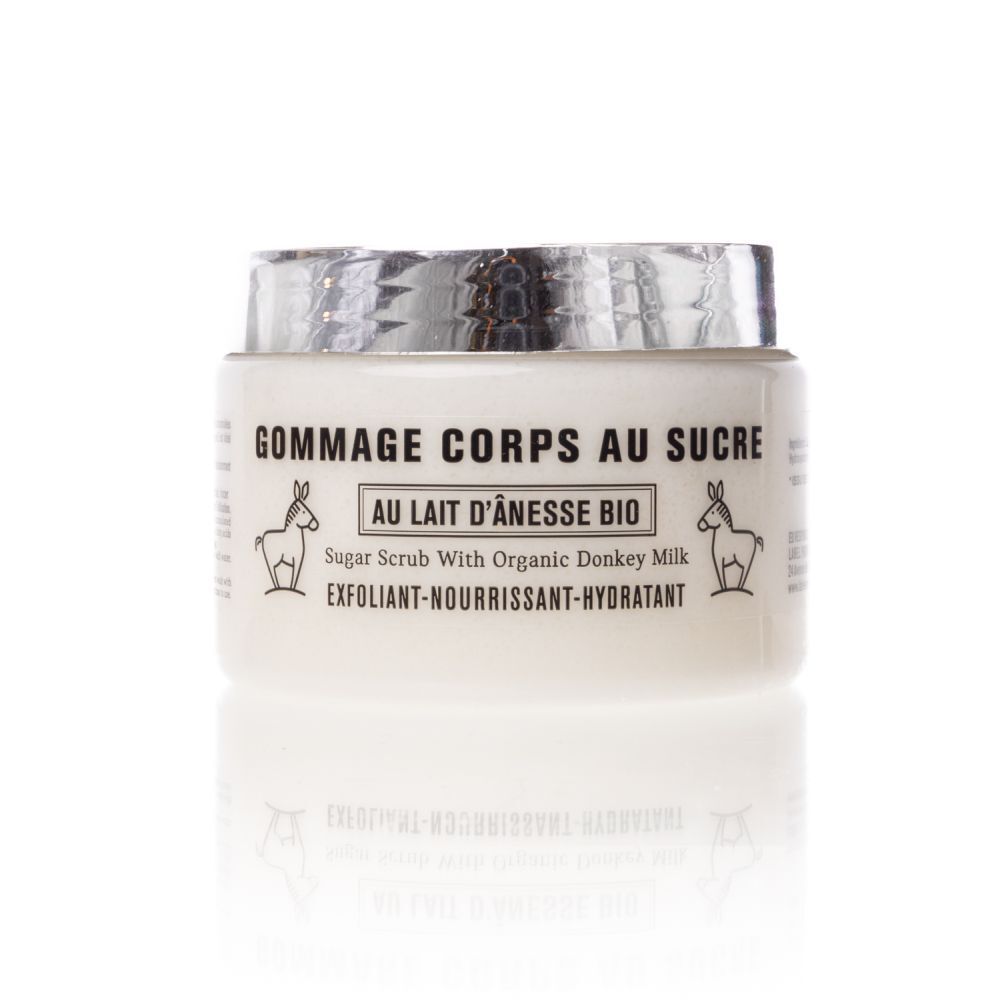 Pot blanc avec couvercle argenté. Inscription: Gommage Corps au Sucre, Au Lait d'Anesse Bio. Avec illustrations d'ânes.
