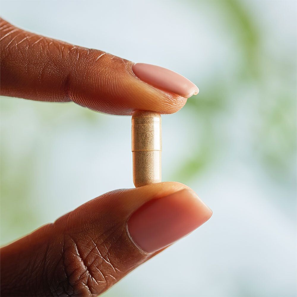 Une gélule tenue entre deux doigts. La gélule est brune et transparente.