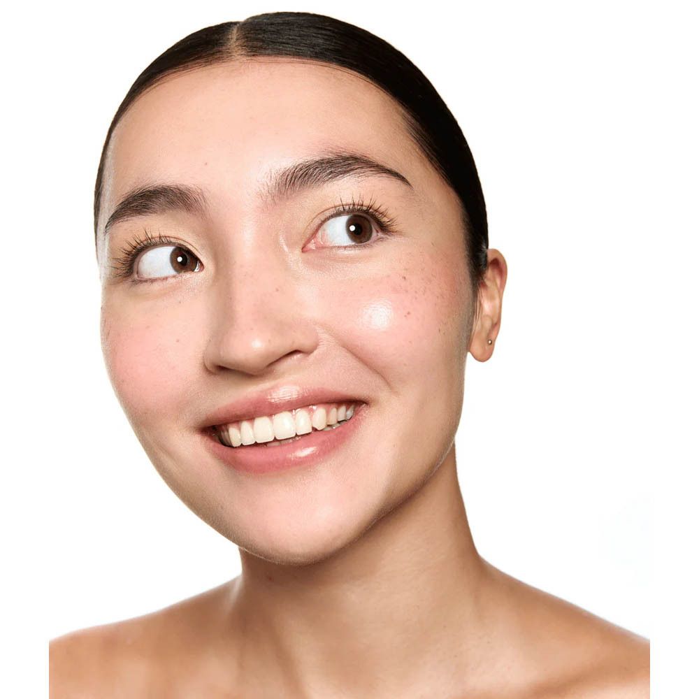 Portrait d'une femme souriante. Elle a les cheveux foncés, la peau claire et un teint naturel. Elle regarde sur le côté.