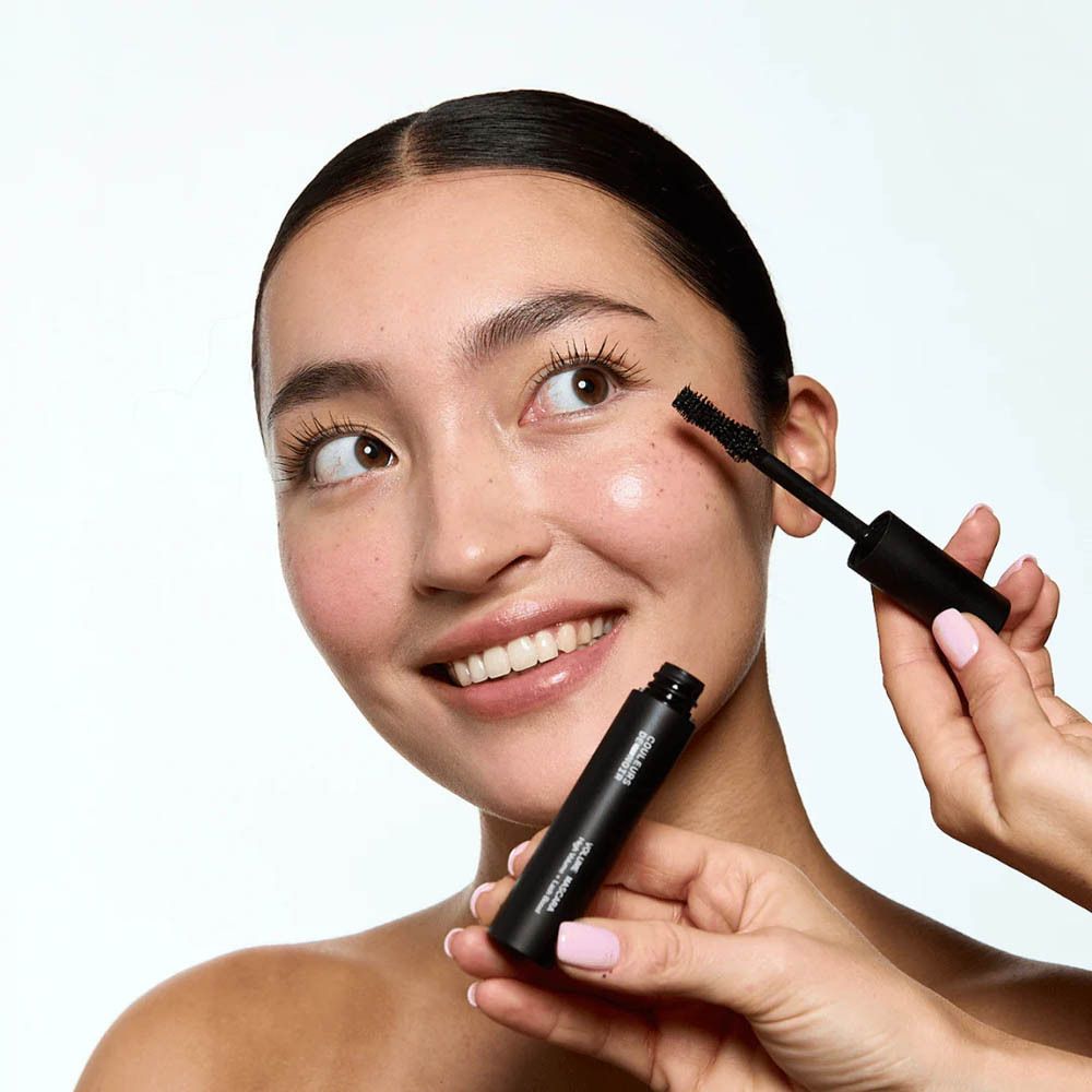 Personne avec applicateur de mascara. Tube de mascara visible.