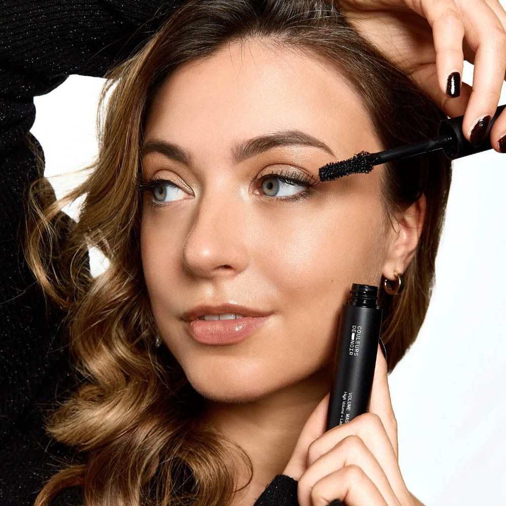 Personne appliquant du mascara. Tube de mascara visible.