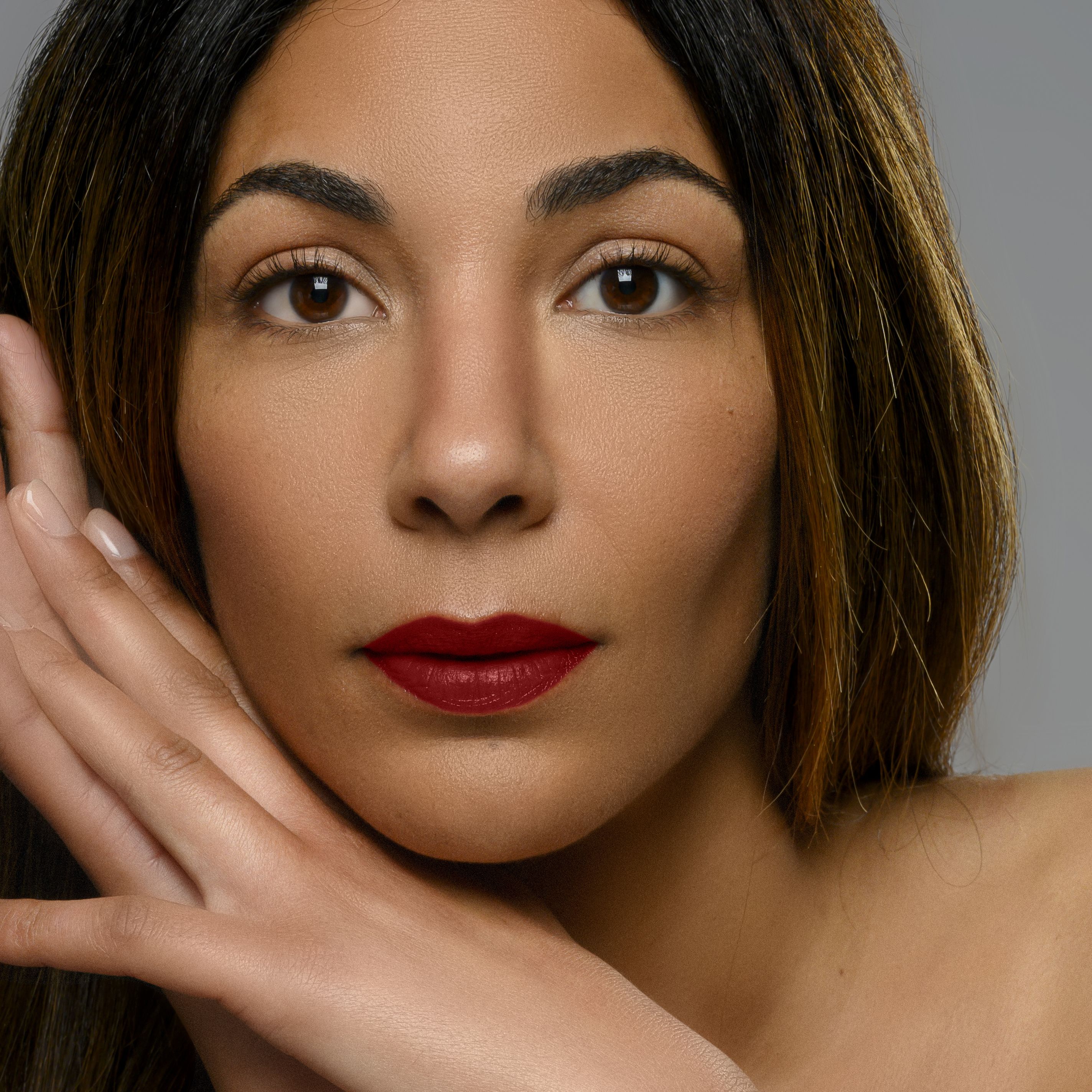 Portrait d'une femme portant du rouge à lèvres rouge. Elle soutient son visage avec ses mains.
