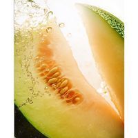 Gros plan d'une tranche de melon avec pépins. L'eau éclabousse la chair. Environnement clair.