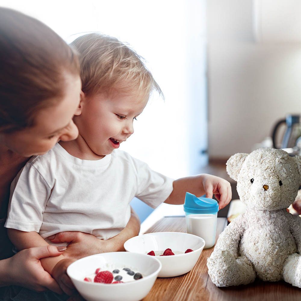 Mère et enfant à table. Bols de nourriture, biberon et ours en peluche.