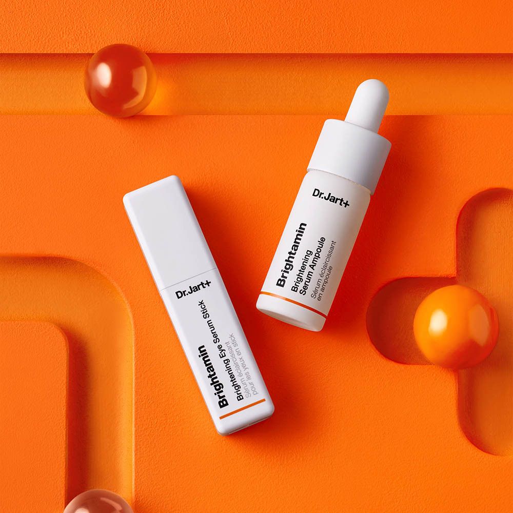 Deux tubes blancs sur fond orange. Inscription : Dr.Jart+ Brightamin Brightening Eye Serum Stick et Ampoule.