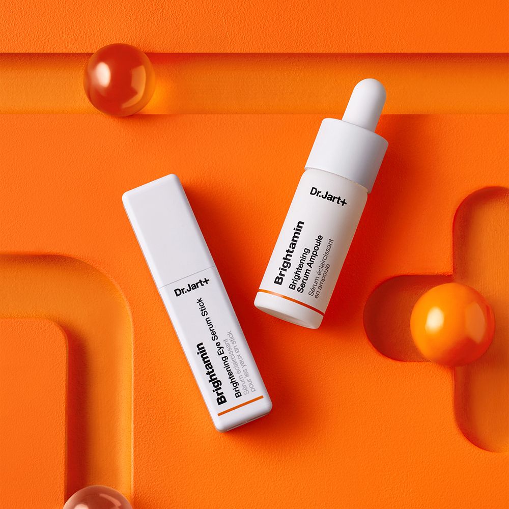 Deux tubes blancs sur fond orange. Inscription : Dr.Jart+ Brightamin Brightening Eye Serum Stick et Ampoule.