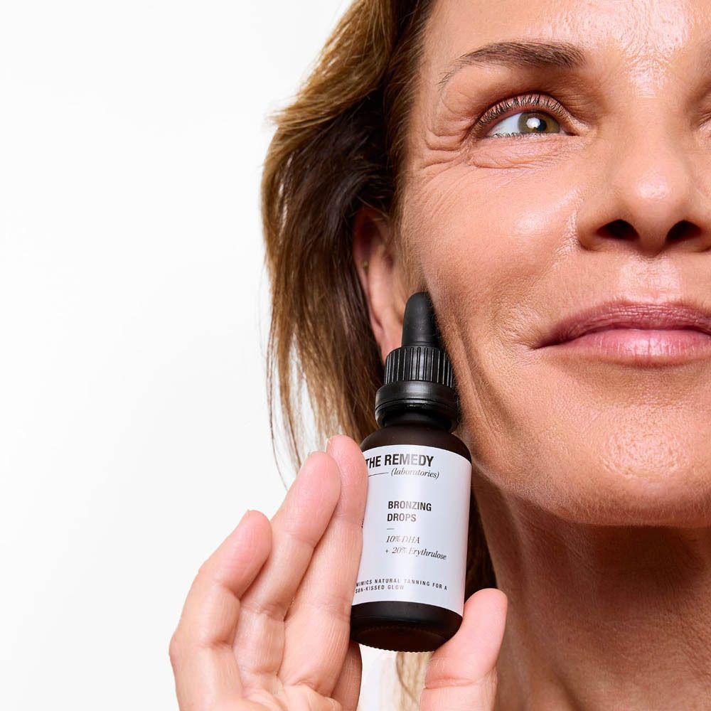 Femme tenant le flacon près du visage. Bronzing Drops. Le compte-gouttes est utilisé sur le visage.