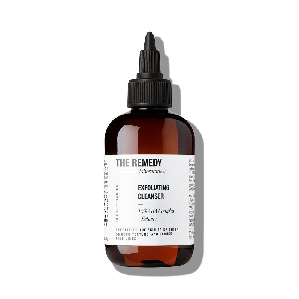 Flacon brun avec bouchon noir. Étiquette avec informations produit. "THE REMEDY" et "Exfoliating Cleanser" sont visibles.