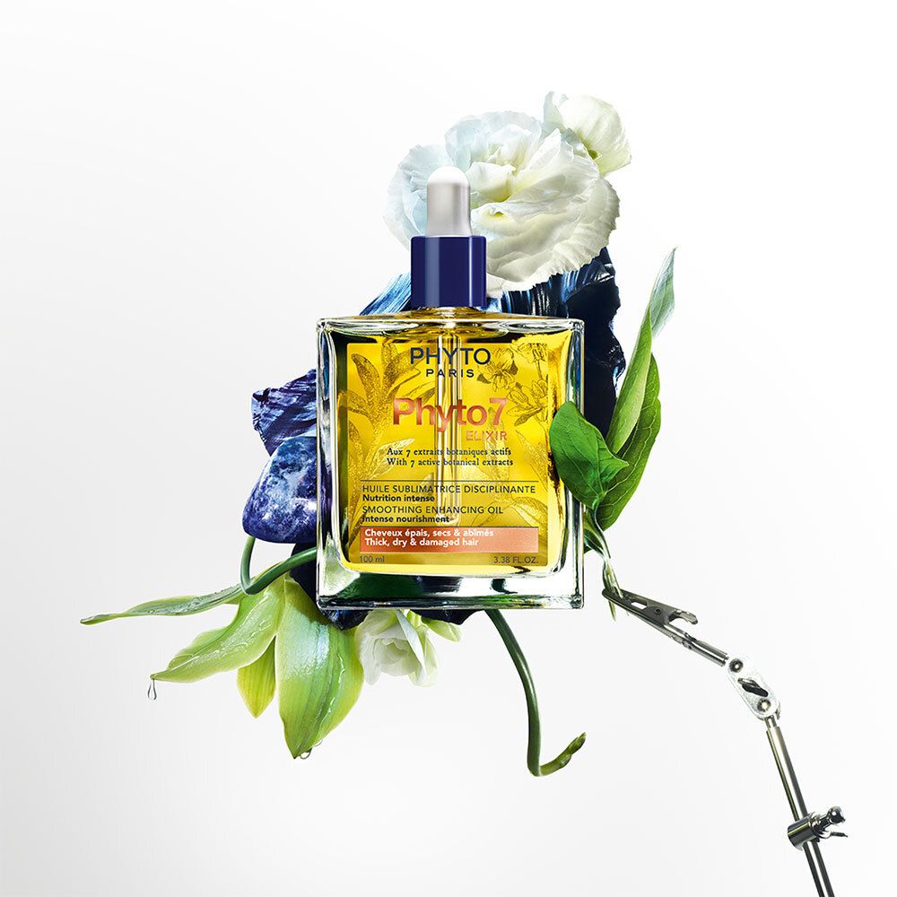 Flacon carré en verre avec huile jaune, entouré de fleurs et de feuilles. Inscription : Phyto Paris, Phyto7 Elixir. Avec compte-gouttes.