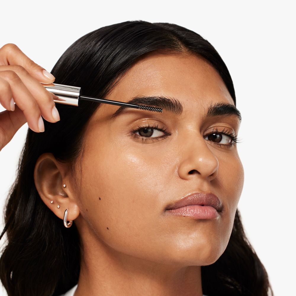 Femme appliquant du gel à sourcils. Brosse en action. Produit non visible.