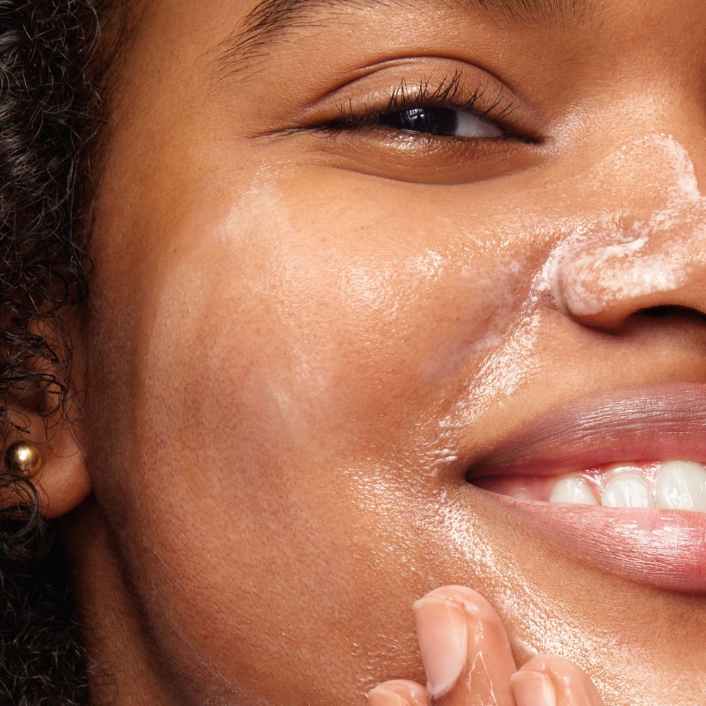 Gros plan d'un visage avec crème sur la peau. Yeux et bouche visibles.