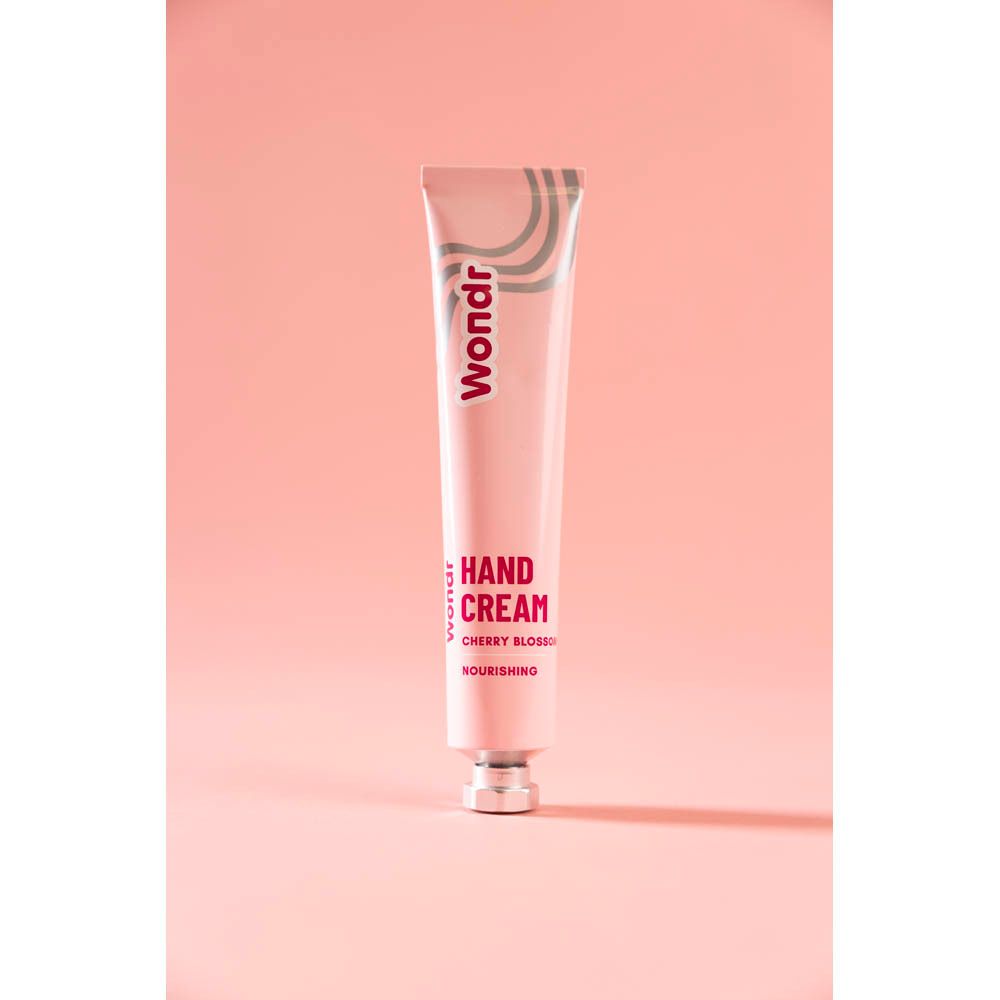 Tube rose avec vagues argentées et logo "Wondr". "Hand Cream Cherry Blossom" et "Nourishing" imprimés.