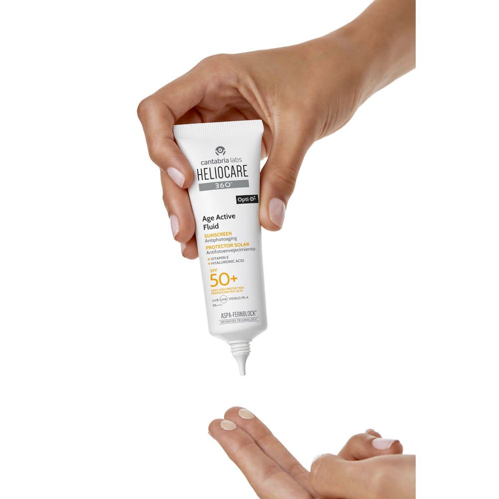 Main tenant un tube blanc. Inscription: Heliocare 360° Age Active Fluid SPF50+. Marque: Cantabria Labs.