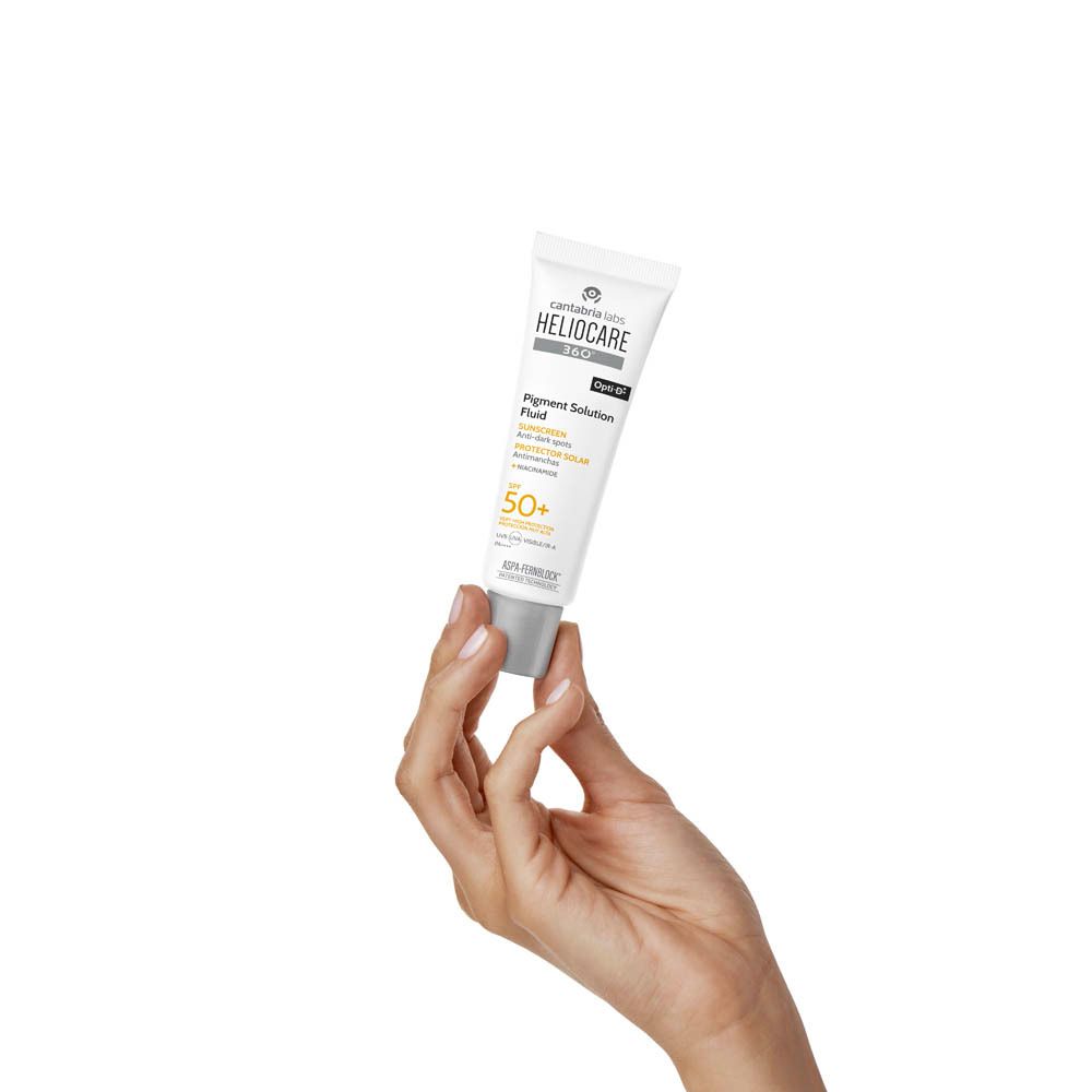 Main tenant un tube Heliocare 360 Fluide Solution Pigment SPF50+. Blanc, avec logo.