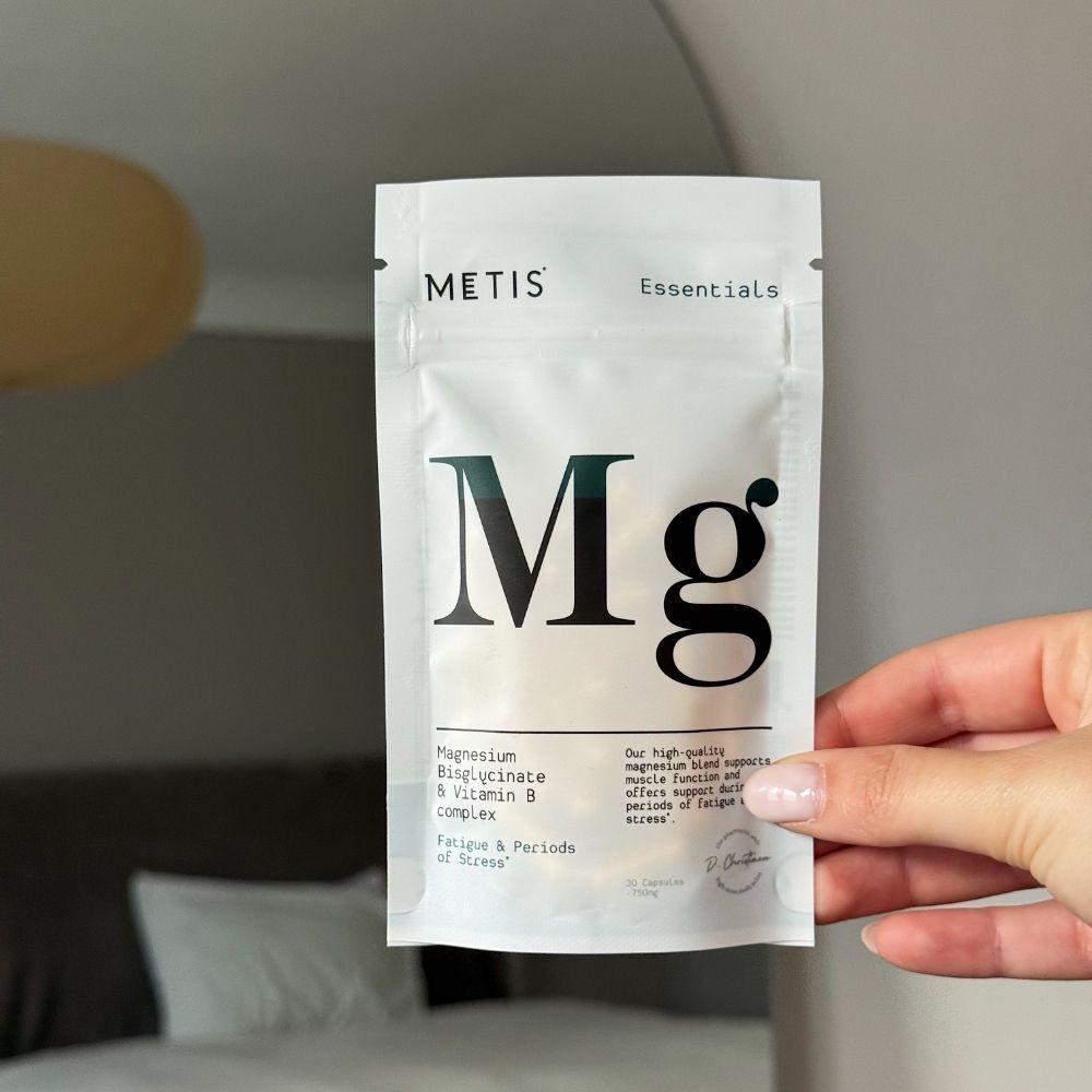 Main tenant un sachet blanc avec "METIS Essentials" et grand "Mg".