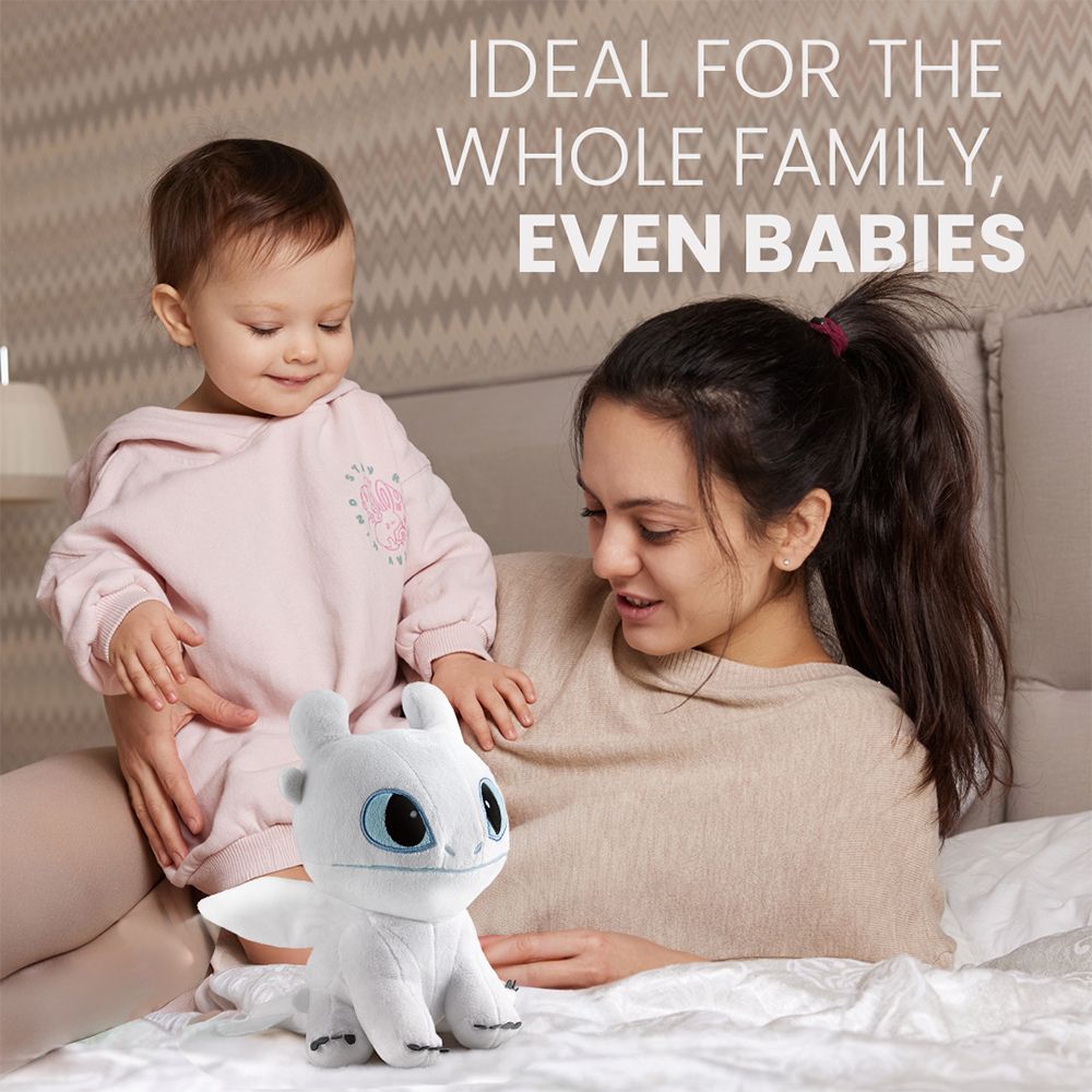 Femme avec bébé câlinant un dragon en peluche blanc sur un lit.