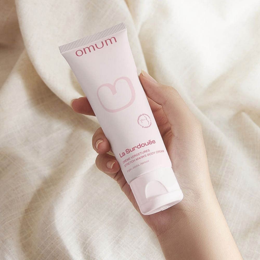 Tube rose avec impression blanche. "omum" en haut. En dessous, "La Surdouée Crème Vergetures".