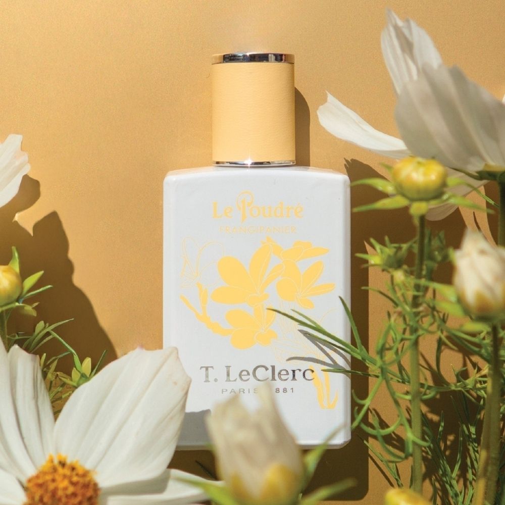 Flacon T. LeClerc Eau de Parfum Le Poudré Frangipanier au milieu de fleurs.