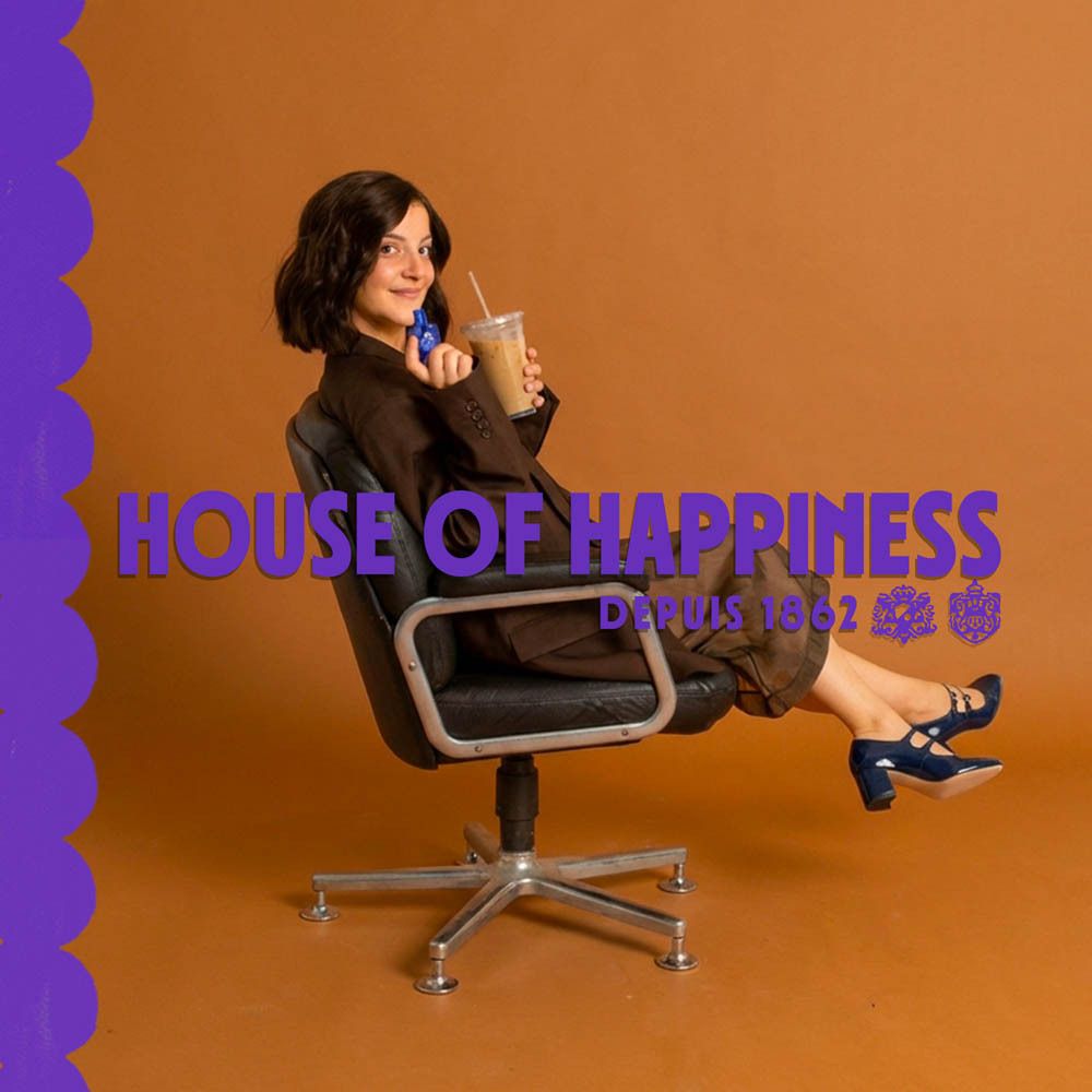 Femme assise avec du café et un parfum roll-on. Texte: House of Happiness, Depuis 1862.