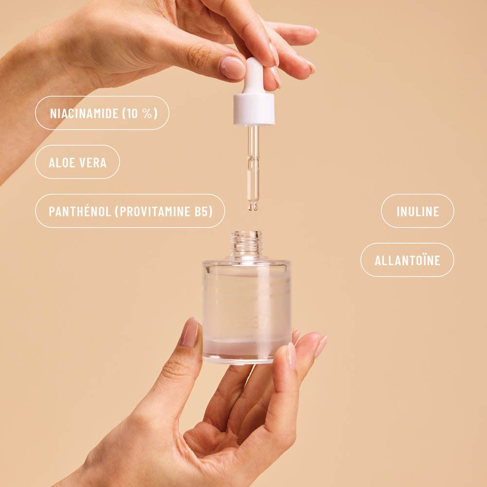 Mains tenant un flacon de sérum avec pipette. Étiquettes : Niacinamide, Aloe Vera, Panthénol, Inuline, Allantoïne.