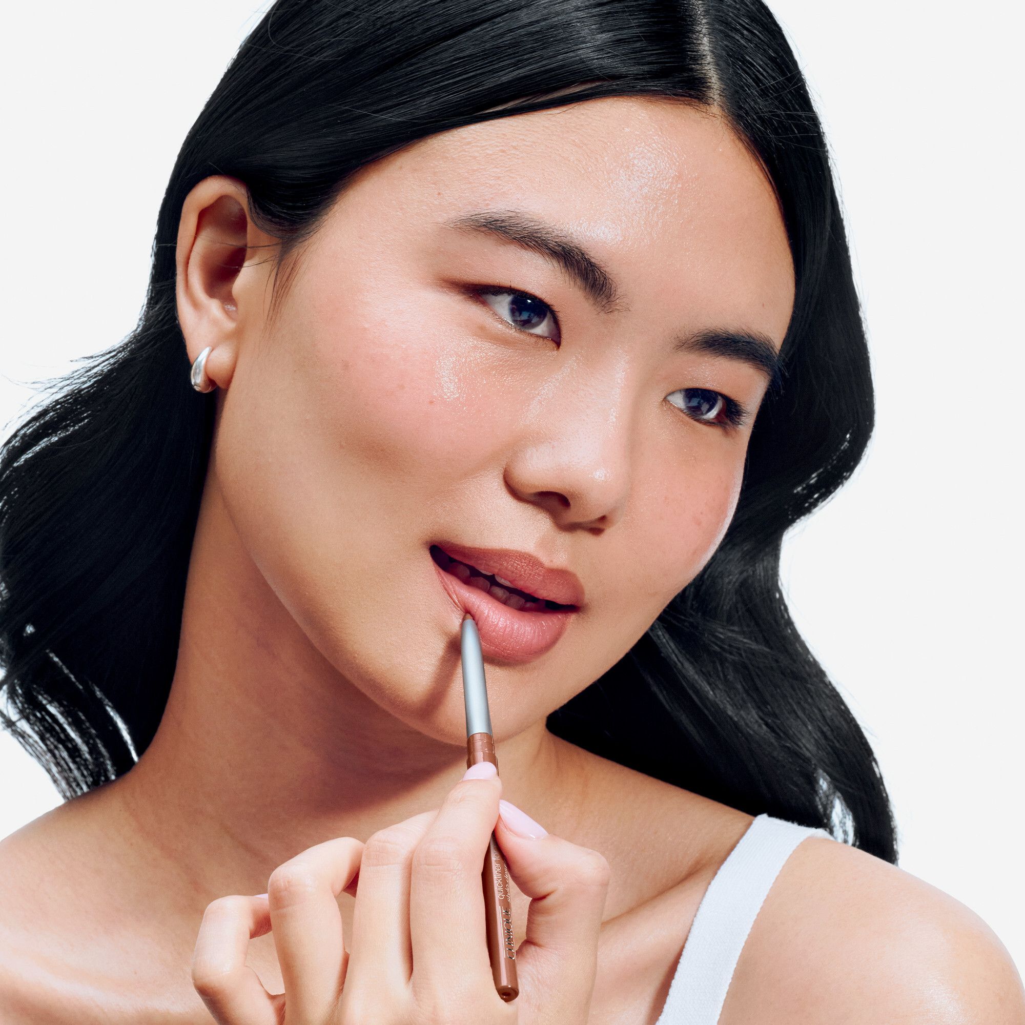 Gros plan d'une femme qui se dessine les lèvres avec un crayon à lèvres brun. Le crayon à lèvres est de Clinique.