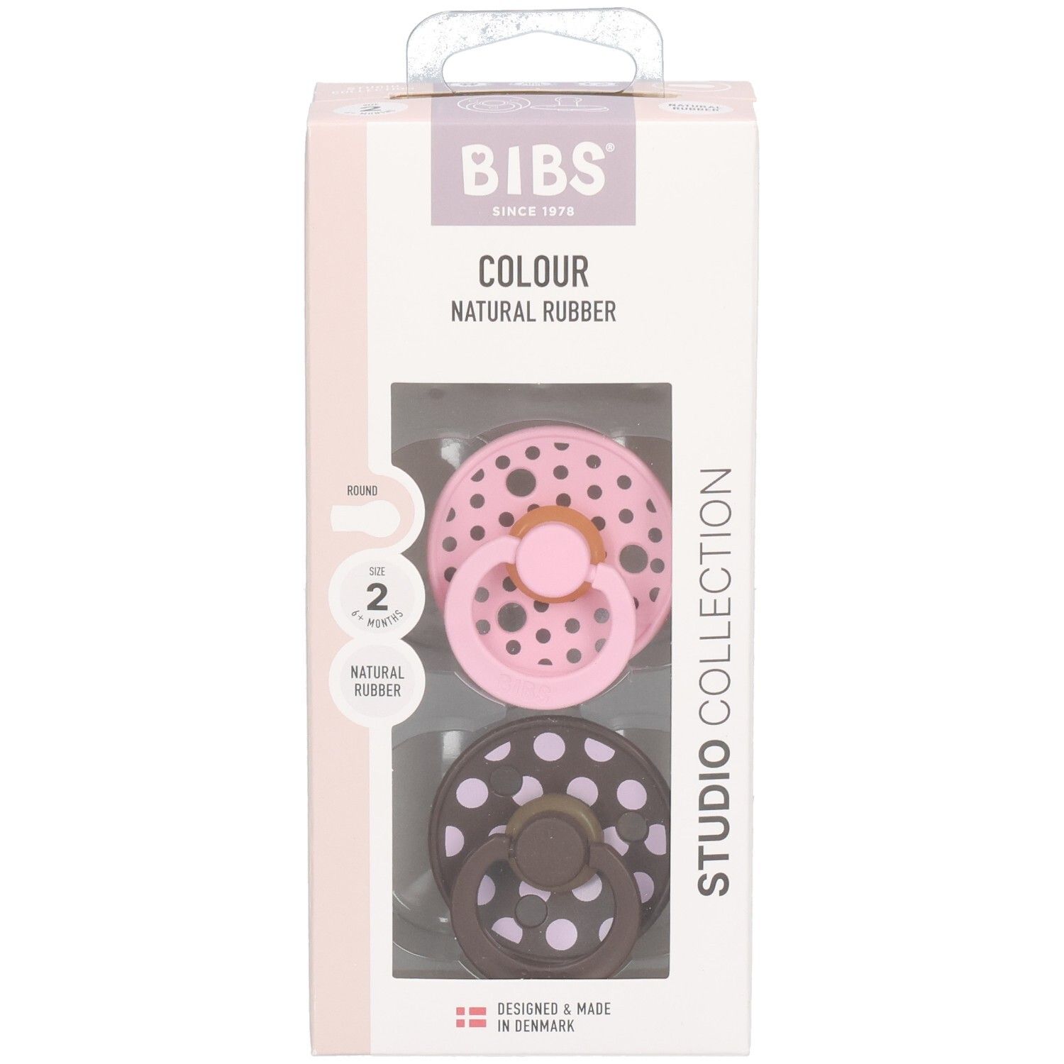 Emballage de deux sucettes. Rose et marron à pois blancs. Marque : BIBS. Texte : Colour, Natural Rubber, Studio Collection.