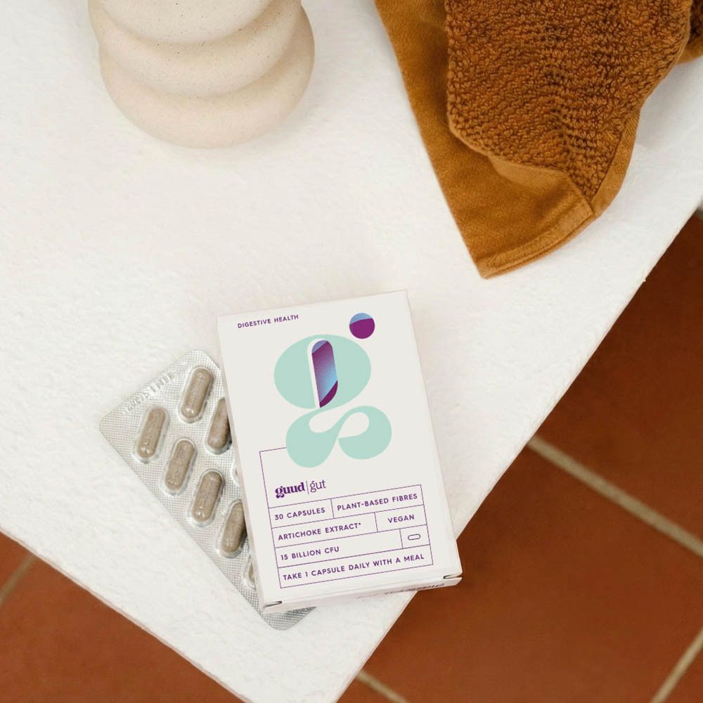 Emballage du produit et blister sur une surface blanche. Inscription : Guud Gut, 30 gélules, fibres végétales, extrait d'artichaut, végétalien.