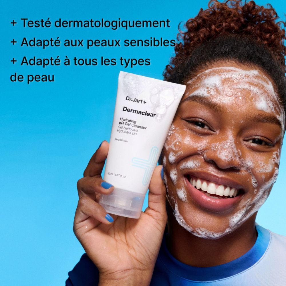 Une femme souriante avec un nettoyant gel moussant sur le visage tient un tube de Dr.Jart+ Dermaclear Hydrating pH Gel Cleanser.