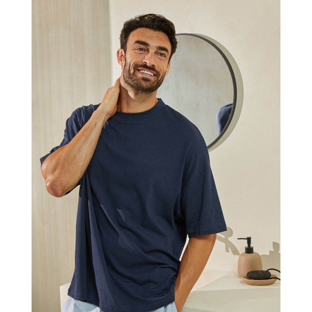 Homme dans une salle de bain, souriant. Porte un t-shirt bleu, miroir en arrière-plan.