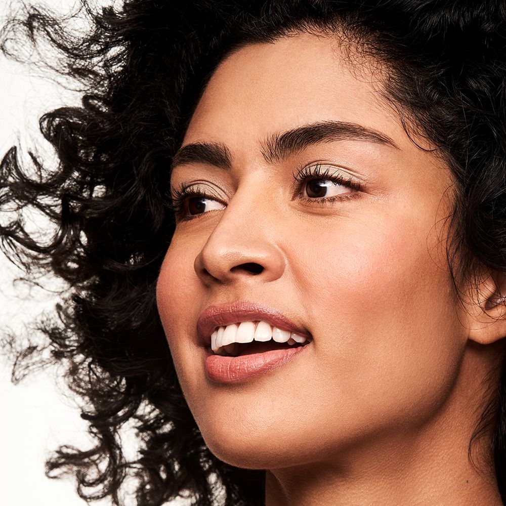 Portrait d'une femme aux cheveux bouclés, regardant au loin. Peau bronzée, lèvres entrouvertes.