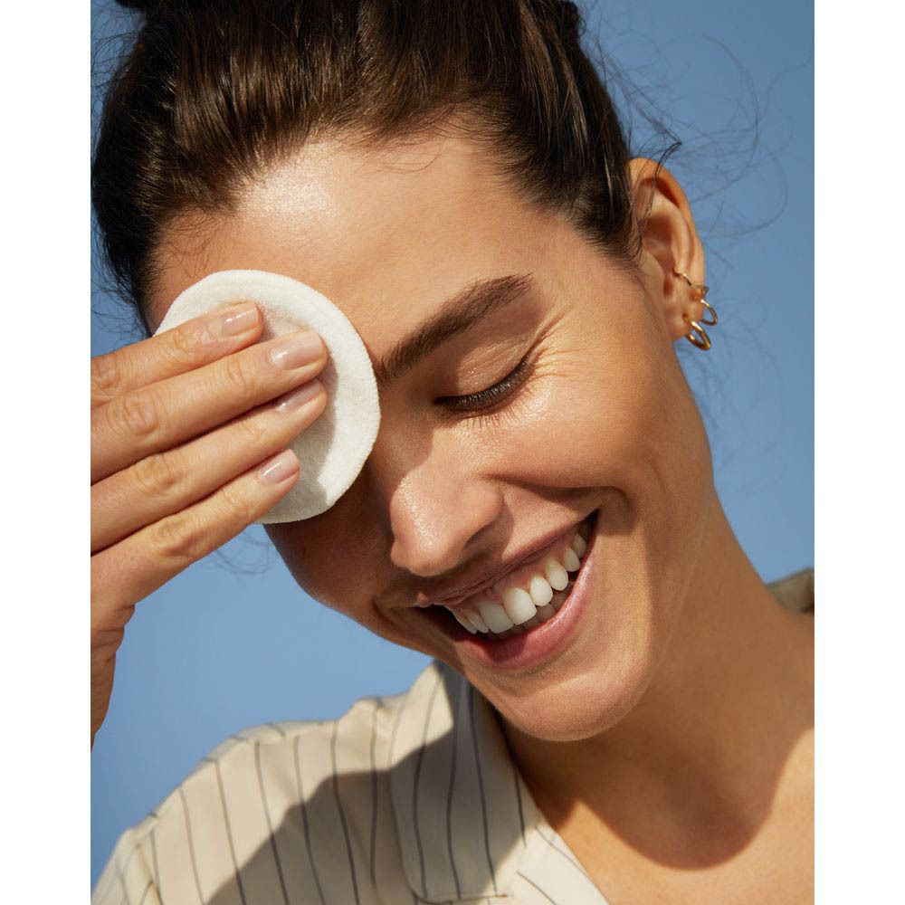 Une femme nettoie son œil avec un coton et de l'eau micellaire NIVEA Rose Care.