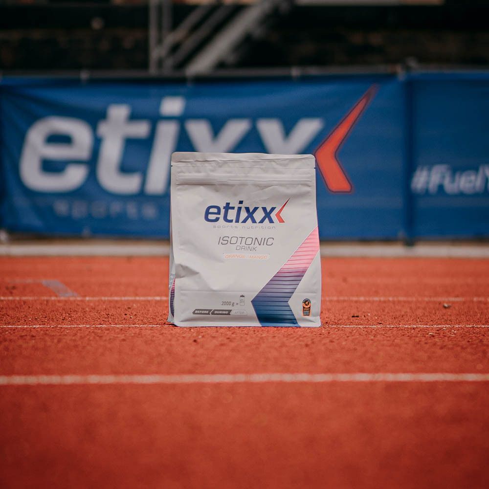 Un sachet Etixx Isotonic Drink Orange-Mango sur une piste de course avec une bannière Etixx en arrière-plan.