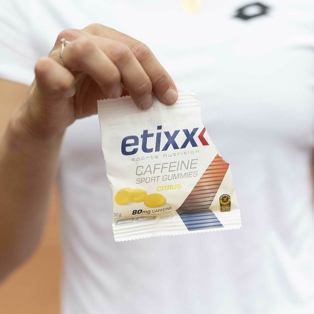 Main tenant un sachet de Etixx Caffeine Sport Gummies. Sachet blanc avec nom du produit, image de bonbons gélifiés jaunes et 80mg caféine.