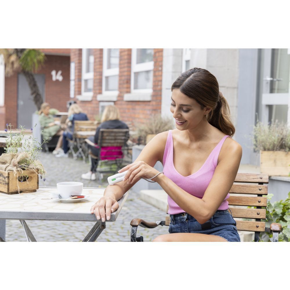 Femme utilise un appareil blanc sur le bras. Table avec café.