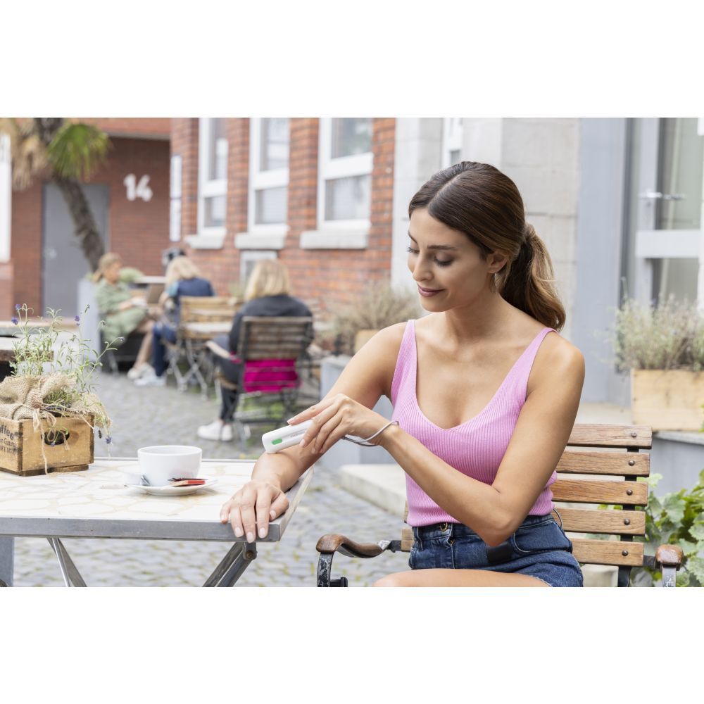 Femme utilise un appareil blanc sur le bras. Table avec café.